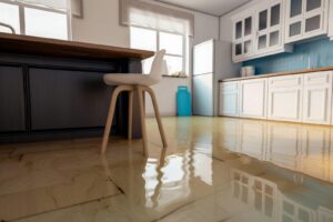 Water flooding the floor of a modern kitchen with white cabinets and a wooden chair.