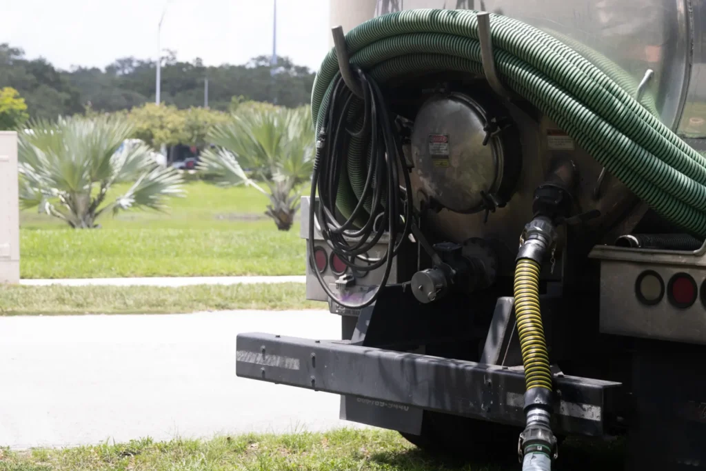 Rear view of a tanker truck with coiled green hoses and a yellow-striped hose attached.
