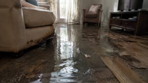 Flooded living room with water covering the floor and damaged wood flooring.