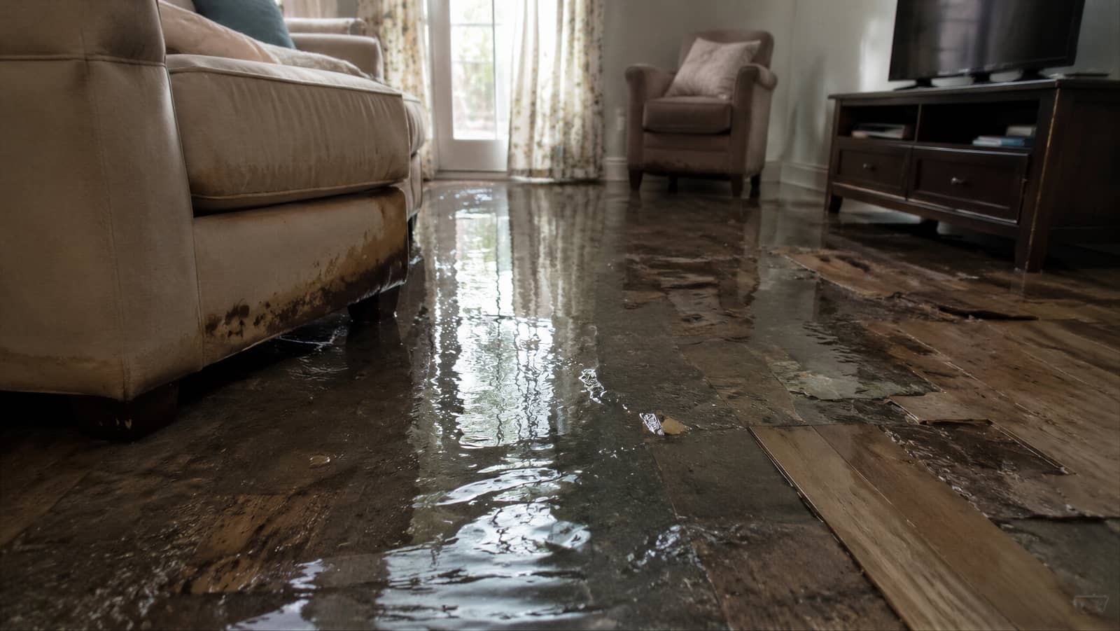 Flooded living room with water covering the floor and damaged wood flooring.