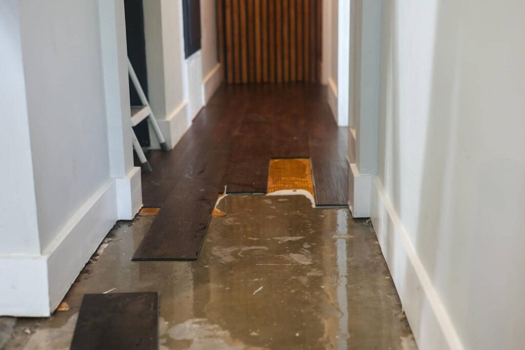 Partially installed dark wood flooring over a concrete subfloor in a hallway.